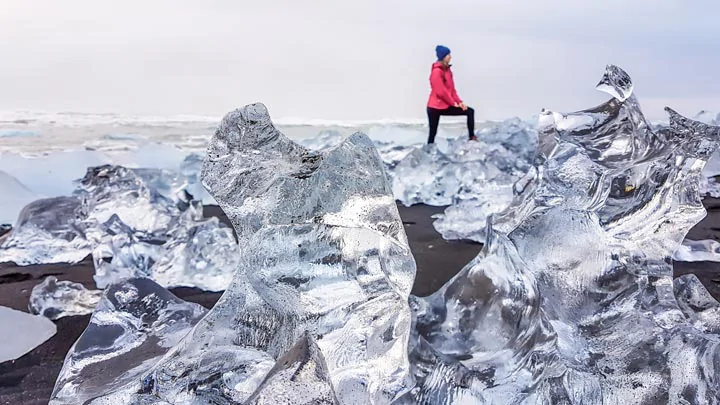 Un touriste marchant sur les blocs de glace de la plage de diamants en Islande